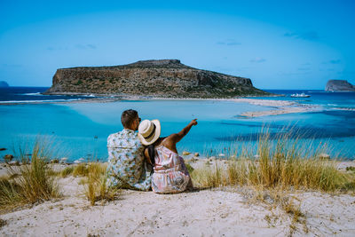 Rear view of woman sitting on beach against sky