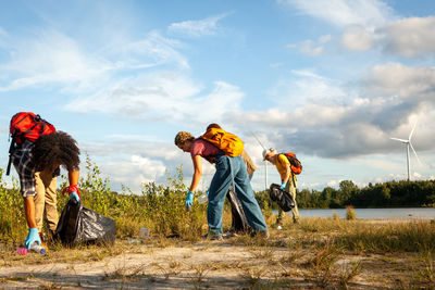 Rear view of friends standing on field against sky