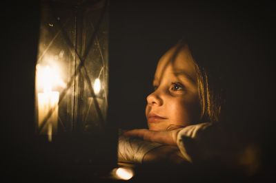 Close-up of girl looking at lit lantern in darkroom