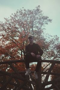 Low angle view of young man sitting against tree