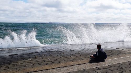 Rear view of woman sitting on sea against sky