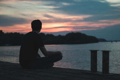 Silhouette man sitting on pier against sky during sunset