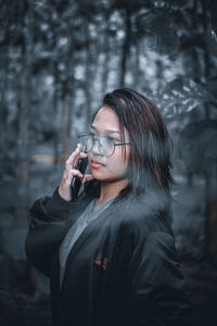 Teenager girl talking on phone while standing against trees