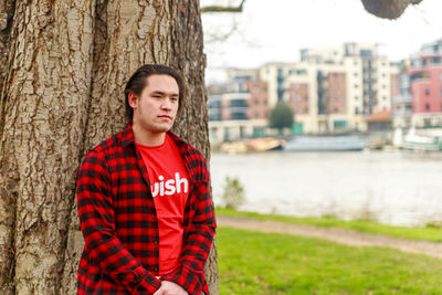 Portrait of a young man standing against tree trunk