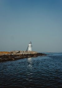 Lighthouse by sea against clear sky