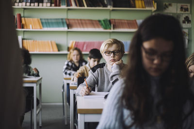 Sad boy with hand on chin sitting at desk in classroom