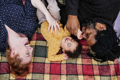 Father and mother playing with son while lying on picnic blanket at park