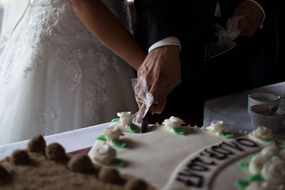 Close-up of young couple cutting wedding cake