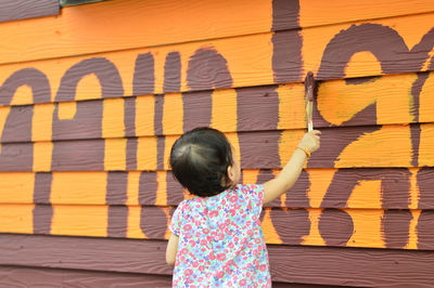 Rear view of girl standing against graffiti wall