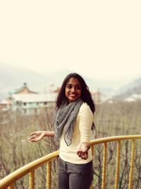 Portrait of smiling young woman standing against railing