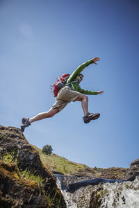 Low angle view of male hiker jumping over stream