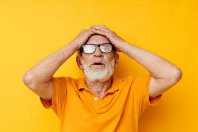 Frustrated senior man against yellow background