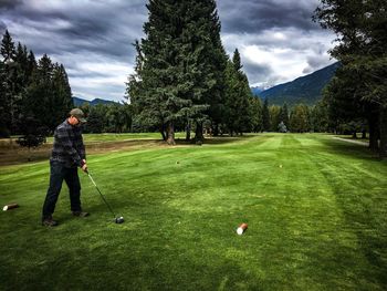 Man playing golf on course against cloudy sky