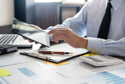 Midsection of businessman using digital tablet at desk in office