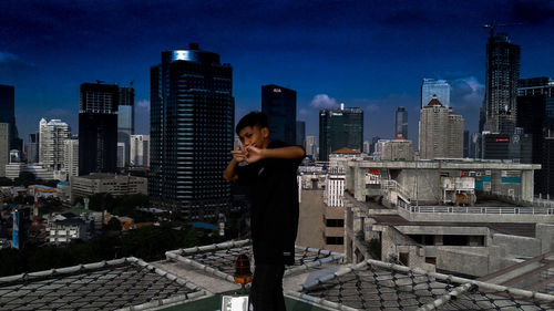 Woman standing by cityscape against clear sky at night