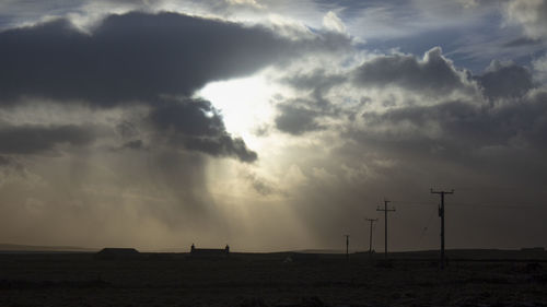 Silhouette electricity pylons on land against sky during sunset