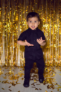 Boy in black clothes at christmas standing in a room on a background of gold tinsel on the wall