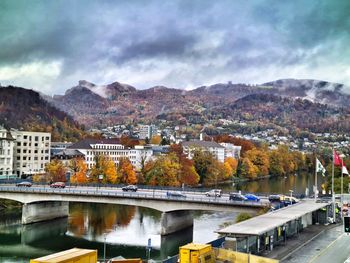 Bridge over river by buildings in city against sky