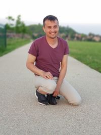 Full length of smiling man looking away while crouching on road