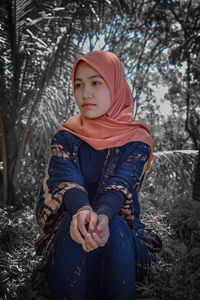 Portrait of woman sitting on field in forest