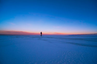 Man standing on snowy landscape against sky during sunset