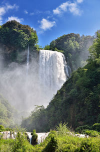 Scenic view of waterfall in forest against sky