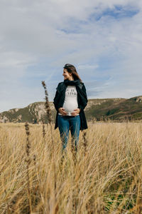 Pregnant woman standing on field against sky