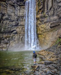 Rear view of man standing on rocks by waterfall