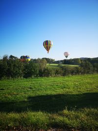 Hot air balloon flying over field against clear sky