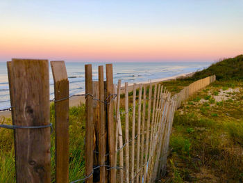 Wooden fence on beach against sky during sunset