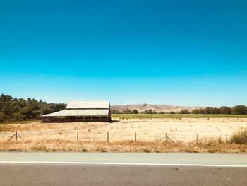 Barn on grassy field against clear blue sky during sunny day