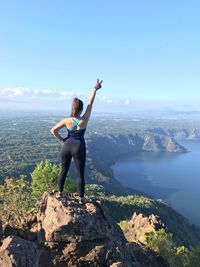 Rear view of woman with hand raised standing on mountain against sky