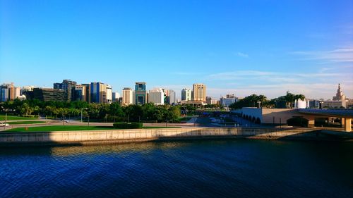 Buildings by river against blue sky