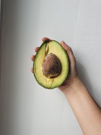 Close-up of hand holding apple against wall