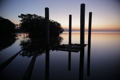 Wooden posts in lake against sky at sunset