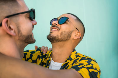 Close-up of gay couple wearing sunglasses romancing against wall