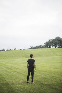 Rear view of young man standing on agricultural field against sky