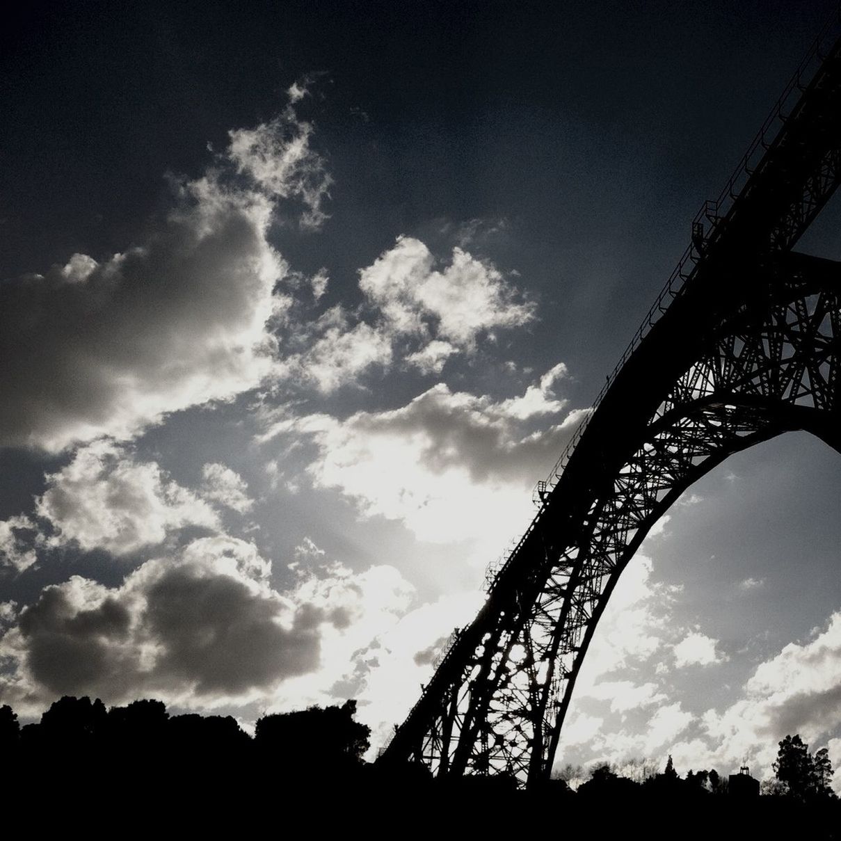 low angle view, silhouette, sky, cloud - sky, built structure, architecture, tree, sunset, cloud, connection, dusk, cloudy, outdoors, no people, nature, engineering, metal, bridge - man made structure, arts culture and entertainment, tranquility