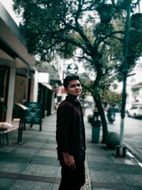 Portrait of young man standing on footpath