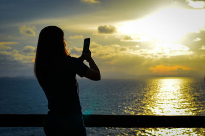 Silhouette woman using smart phone against sea during sunset