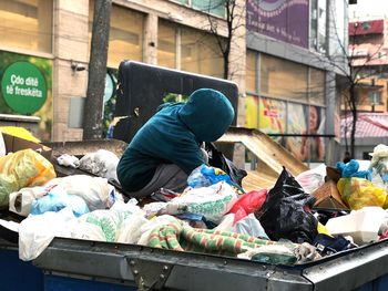 Person crouching on garbage in bin