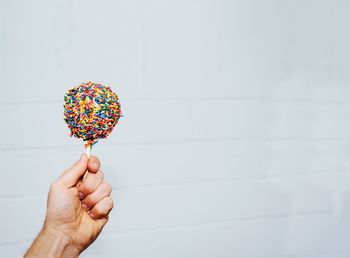 Cropped hand of man holding sweet food by white wall