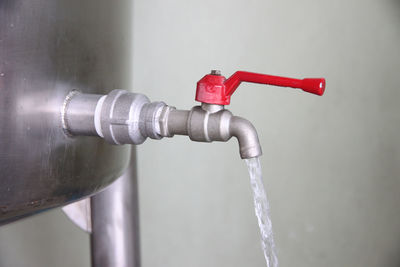 Close-up of water running from faucet on metallic container in industry