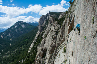 Person climbing cliff against sky