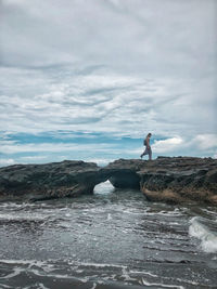 Man walking on rock by sea against sky