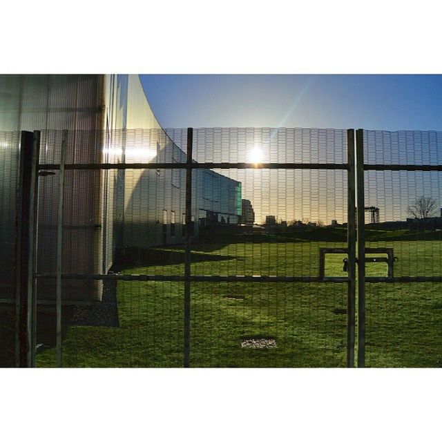 fence, protection, safety, grass, chainlink fence, built structure, security, architecture, building exterior, window, sunlight, sky, metal, pattern, day, glass - material, no people, metal grate, green color, transfer print