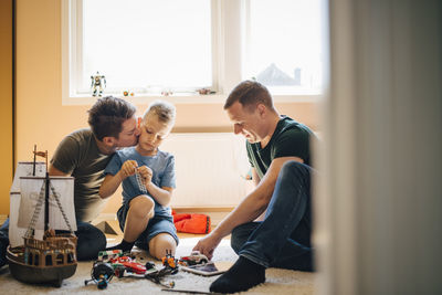 Father kissing son while teaching toy boat at home