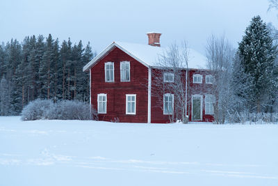 House on snow covered field by building against sky