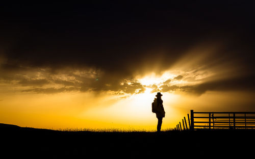 Silhouette man standing on field against sky during sunset
