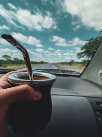 Midsection of person holding glass of car against sky